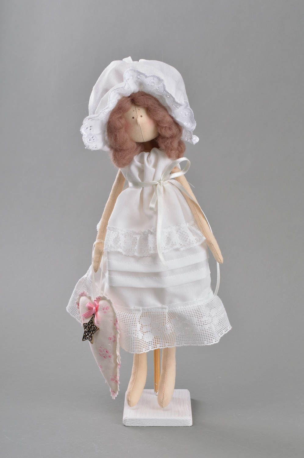 Handmade cute toy doll made of fabric in white dress and bonnet on stand photo 2