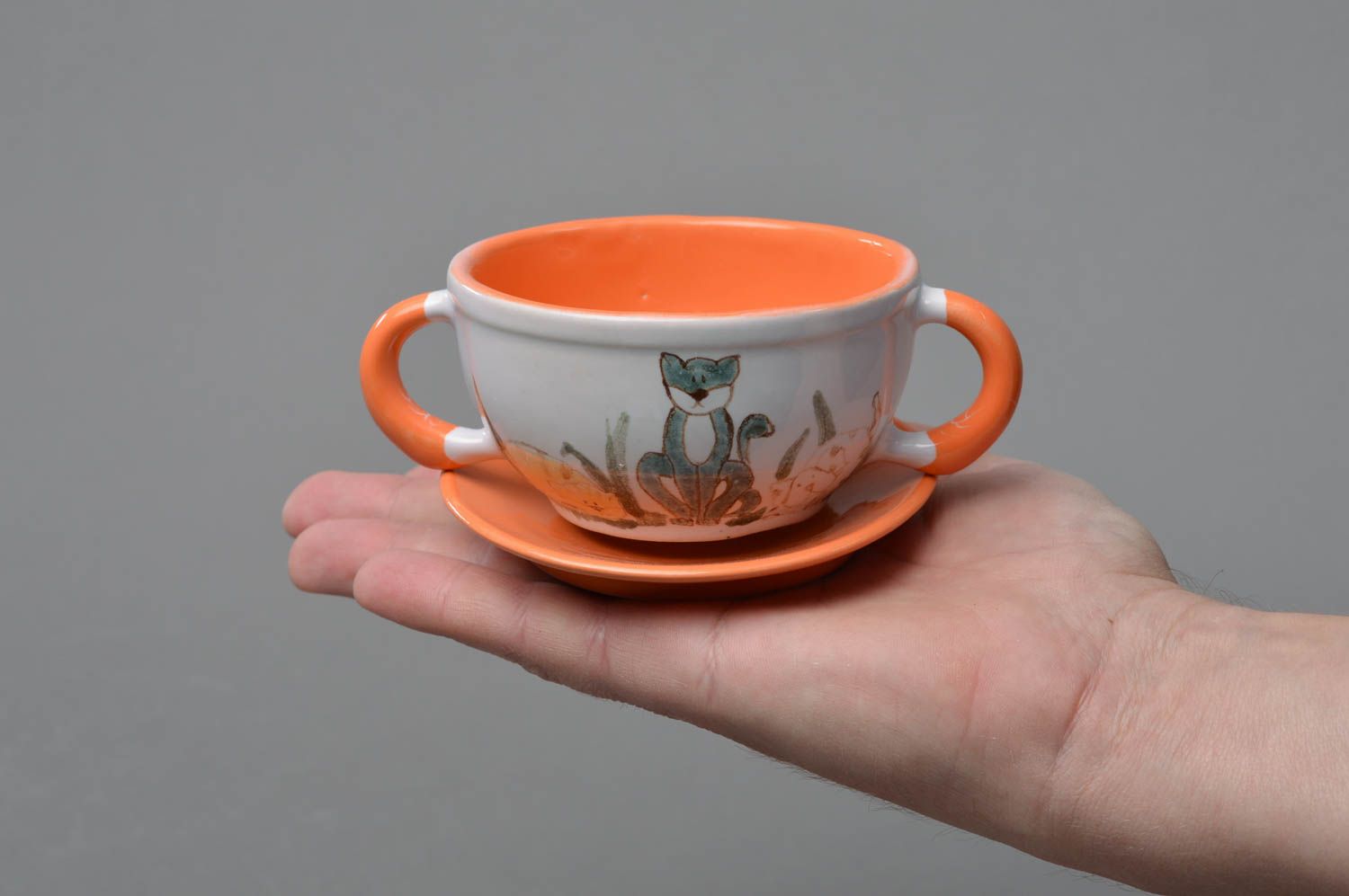 Small kids' ceramic tea cup in white and orange colors with two handles, saucer, and kitty pattern photo 4