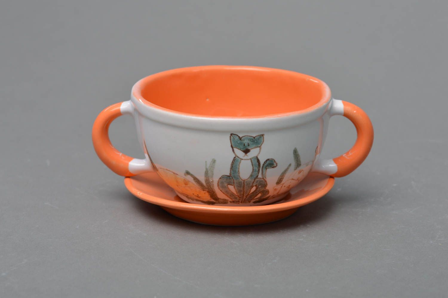 Small kids' ceramic tea cup in white and orange colors with two handles, saucer, and kitty pattern photo 1