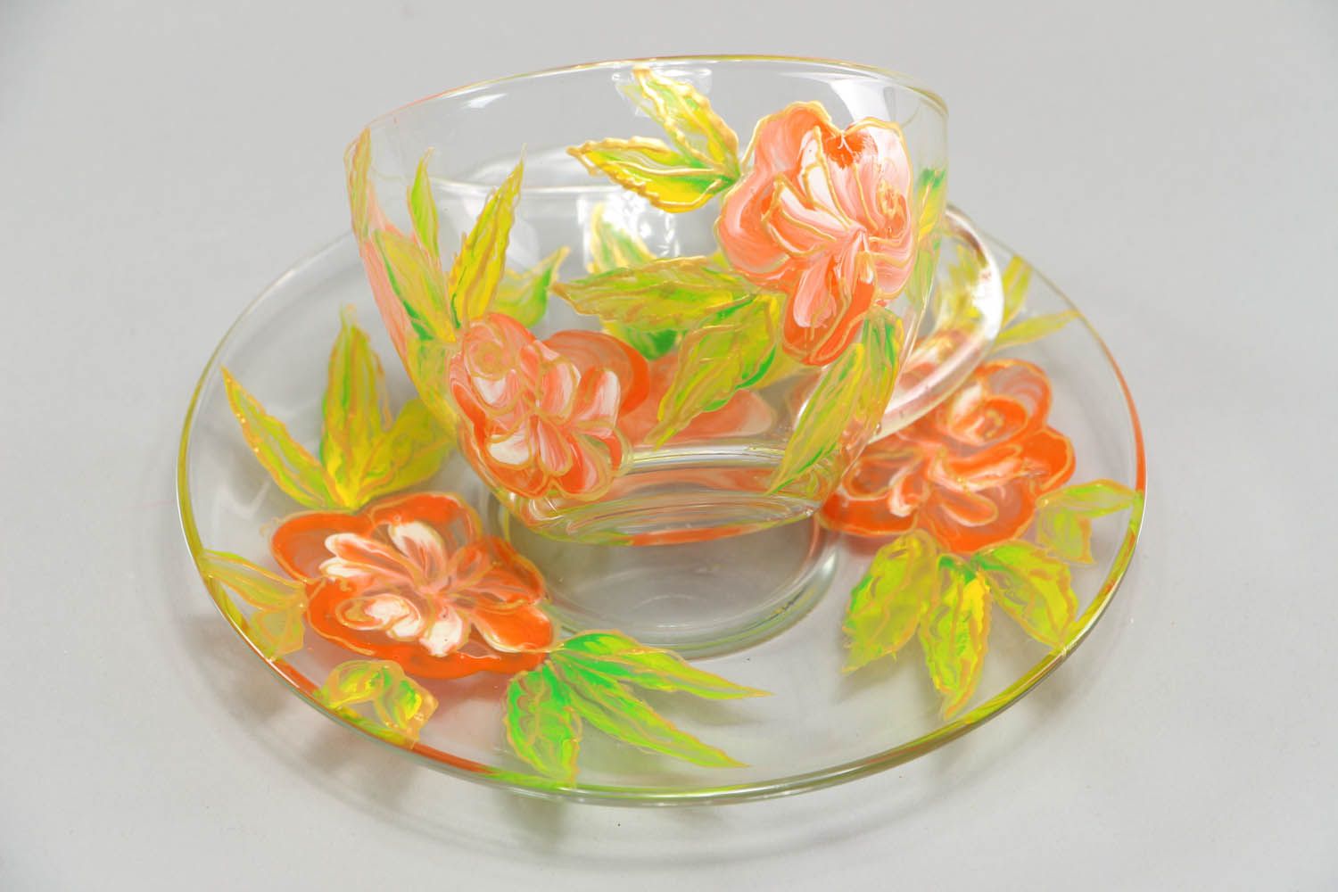 Clear glass tea cup with handle, saucer, and red and yellow flower pattern photo 1