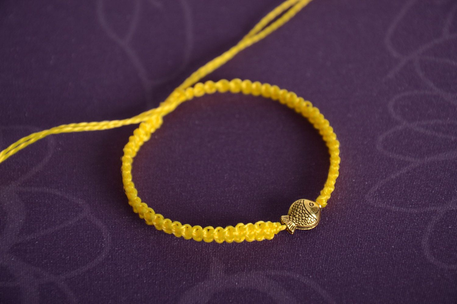 Handmade women's designer macrame woven bracelet of yellow color with metal charm in the shape of fish photo 1
