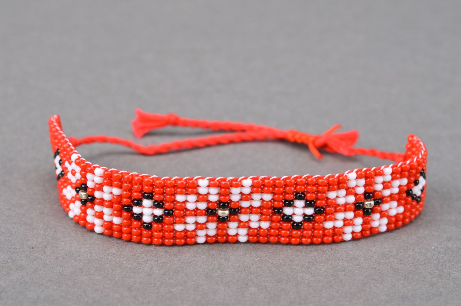 Handmade red beaded wrist bracelet with ties and white flower pattern photo 1