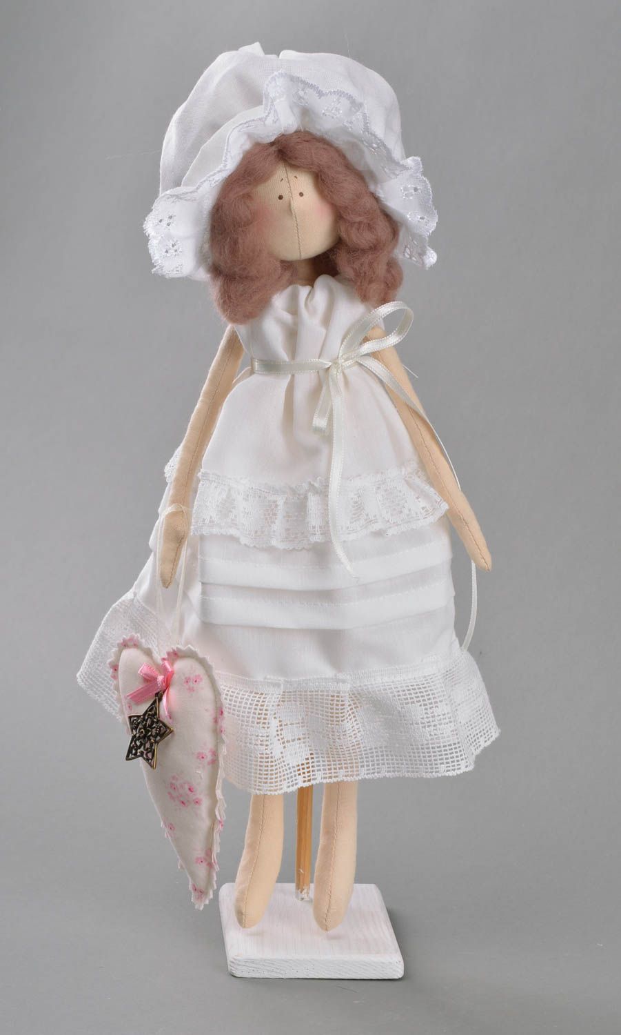 Handmade cute toy doll made of fabric in white dress and bonnet on stand photo 1